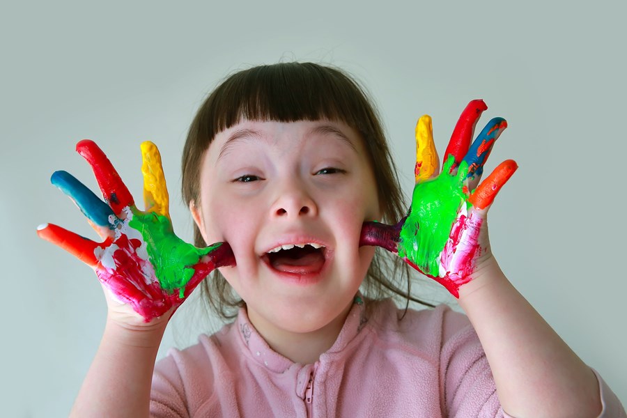 Photo image of a child looking into the camera showing their hand covered in different coloured paint (Shutterstock image)