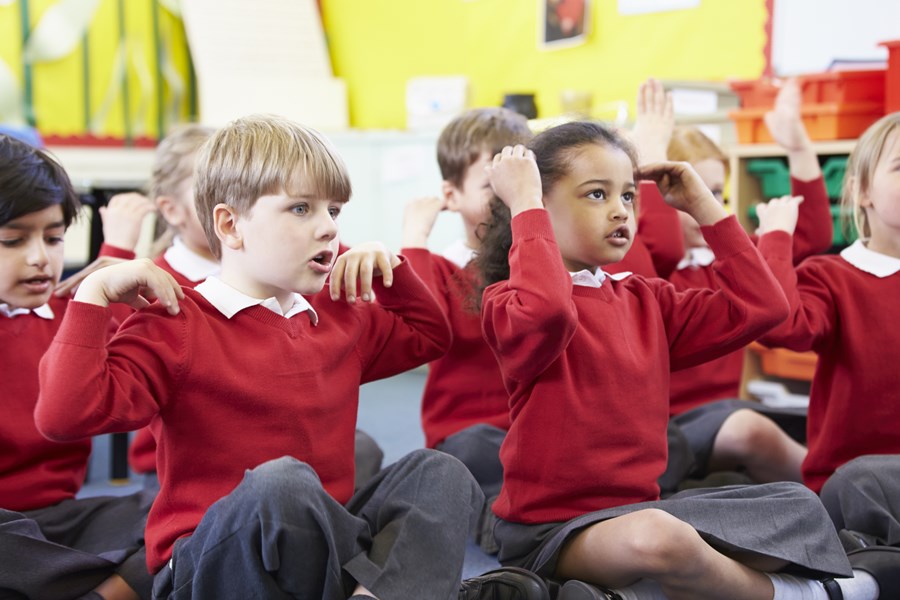 Photo image of children in a classroom sitting on the floor moving their arms for exercise (Shutterstock image)