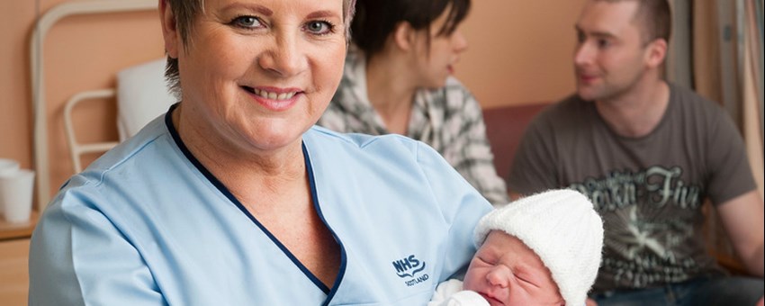 Maternity Clinical Support holding newborn baby, parents in background