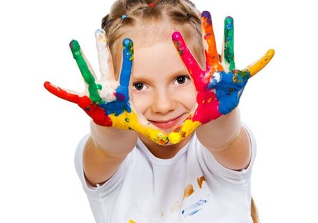 Photo image of a child looking into the camera with their hands reaching forwards covered in different colours of paint (Shutterstock image)