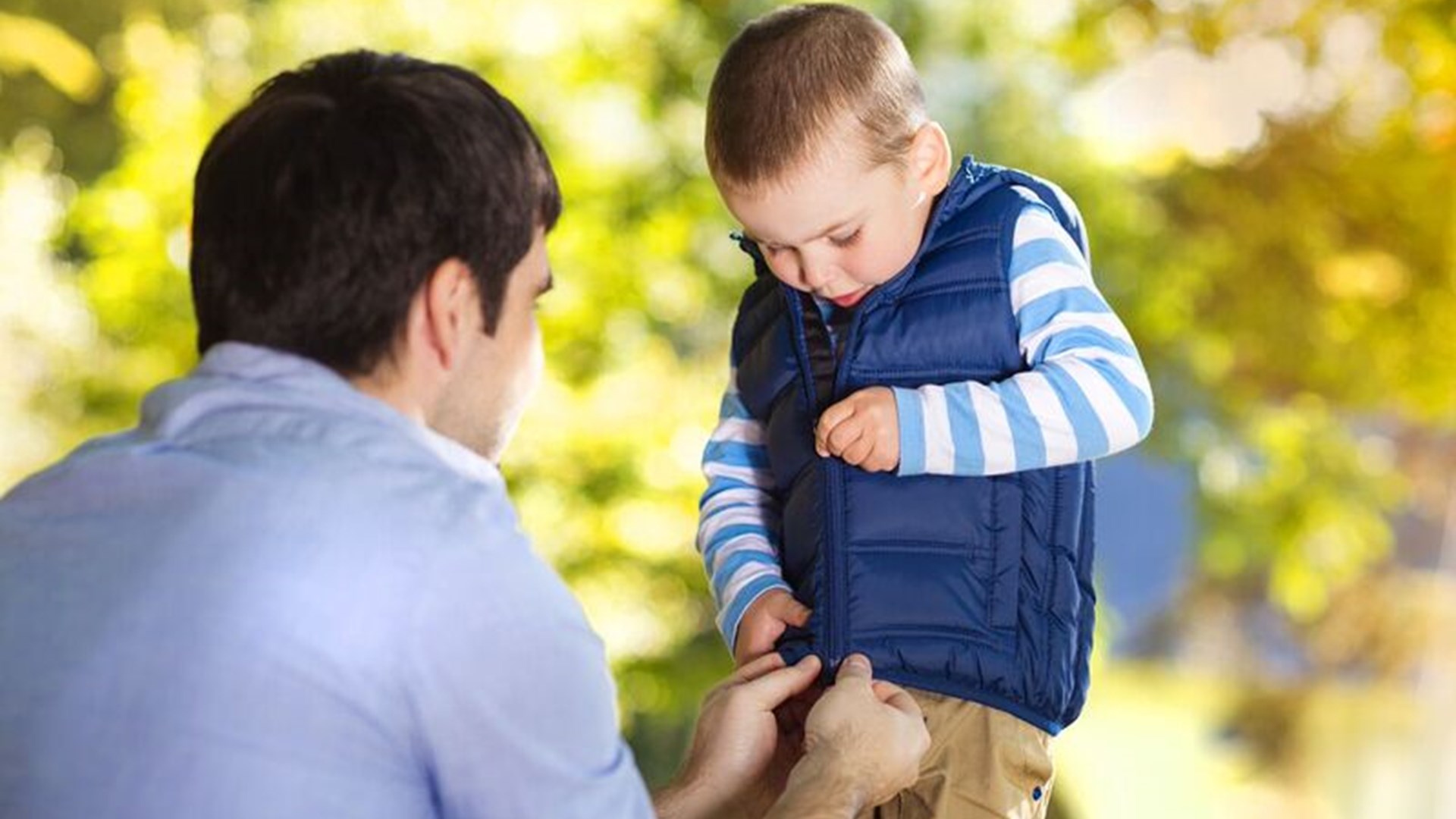 Photo image of an adult helping a child pull up a zip up on a body warmer (Shutterstock image)