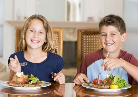 Photo image of two children eating their dinner with forks looking directly to the camera (Shutterstock image)