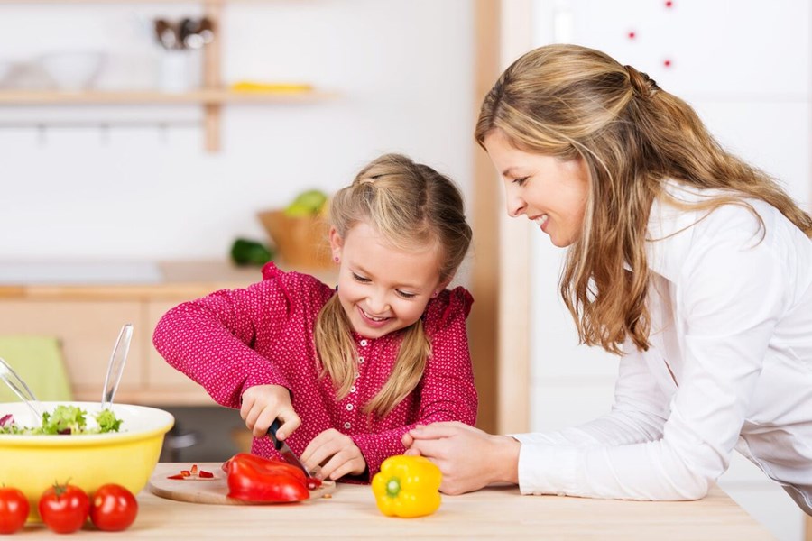 Photo image of a child and an adult slicing peppers in a kitchen (Shutterstock image)