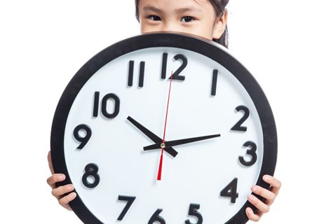 Photo image of a child holding a very big analogue clock (Shutterstock image)
