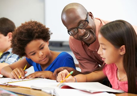 Photo image of two children and a teacher looking and discussing their school work (Shutterstock image)