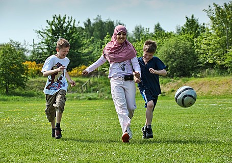 Photo image of an adult and teenagers playing football in a park